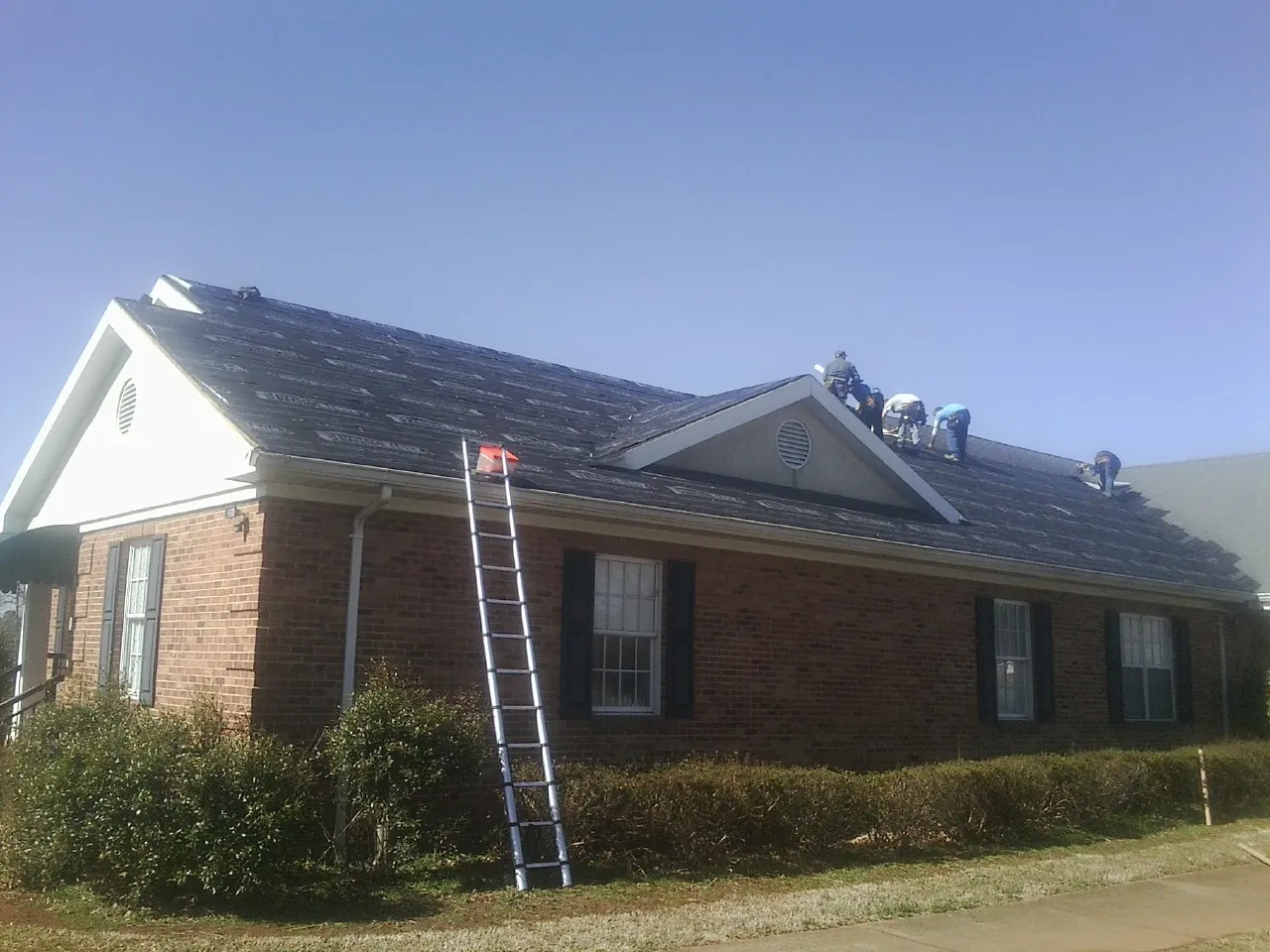 Crew tearing shingles off a brick ranch roof with a ladder set — Metal Roof Repair work by our crew in Leesville